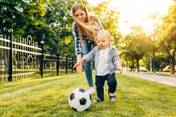 Happy young mom and her little son play soccer together outdoors