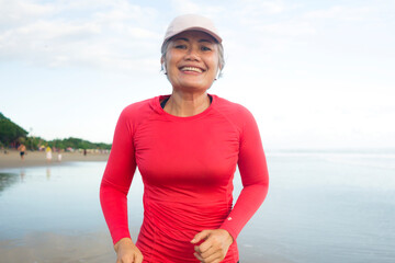 Fototapeta premium fit and attractive mature woman with grey hair doing beach workout on her 50s running on the beach happy and free in senior fitness selfcare and wellness concept