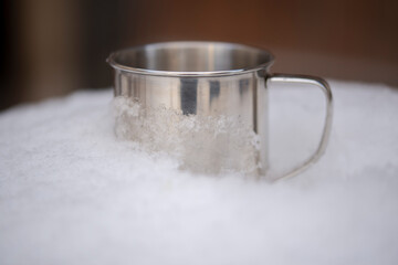Metal tourist mug for hot drinks in white snow. The concept of tourism in winter