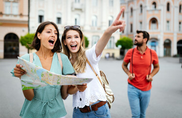 Holidays, travel, friends and tourism concept. Beautiful girls looking into tourist map in the city