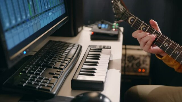 Close up male hands of musician recording song in record studio. Man playing guitar and synthesizer creating music using equalizer program.