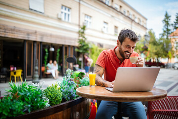 Young man having fun, enjoying free time on laptop and smiling while sitting in cafe