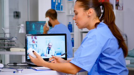 Resident physician talking to doctor on video call during virtual meeting, listening medical advice and taking notes. Remote healthcare service, video health conference, telemedicine online webinar.