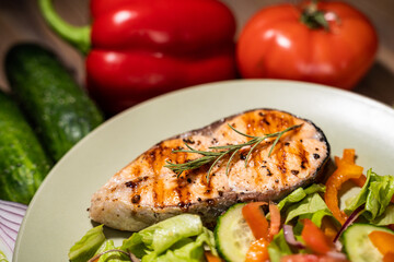 plate of grilled salmon steak with vegetables on wooden table, top view