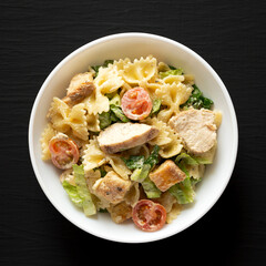 Homemade Chicken Caesar Pasta Salad in a white bowl on a black surface. Flat lay, overhead, from above.