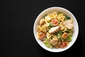 Homemade Chicken Caesar Pasta Salad in a white bowl on a black background, top view. Flat lay, overhead, from above. Space for text.