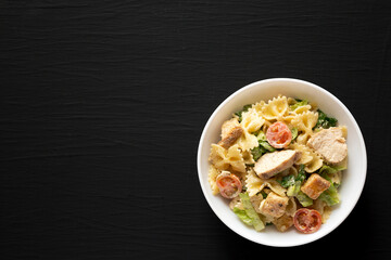 Homemade Chicken Caesar Pasta Salad in a white bowl on a black background, top view. Flat lay, overhead, from above.