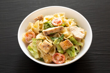 Homemade Chicken Caesar Pasta Salad in a white bowl on a black background, side view.