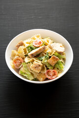 Homemade Chicken Caesar Pasta Salad in a white bowl on a black background, side view.