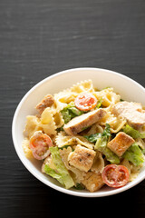 Homemade Chicken Caesar Pasta Salad in a white bowl on a black surface, side view. Copy space.