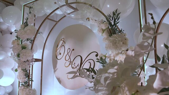 Middle shot of beautiful photo zone. Elegant and stylish decoration for any event. Celebrate your wedding with wonderful decor. White baloons, flowers, roses, metal construction, arch, pompous
