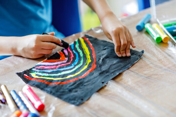 Closeup of child painting rainbow picture with different stick colors on black background during...