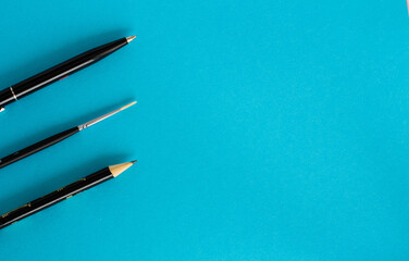 Black pen, pencil and paintbrush on blue background