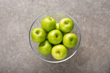 Ripe green apples in a bowl on a gray background, top view