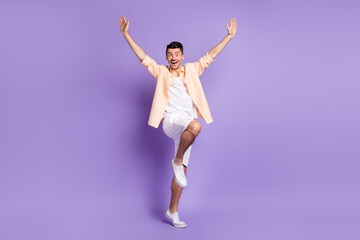 Full length photo of dancer guy raise hands wear beige shirt white shorts sneakers isolated purple color background