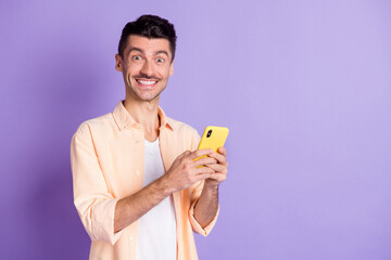 Photo of optimistic brunet guy hold telephone wear peach shirt isolated on lilac color background