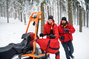 Paramedics from mountain rescue service provide operation outdoors in winter in forest.