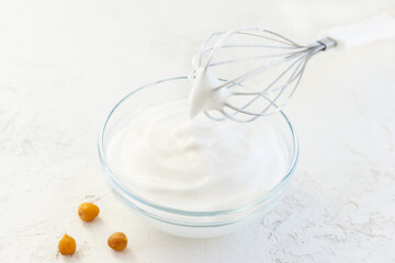 Whipped aquafaba in a glass bowl with a whisk.