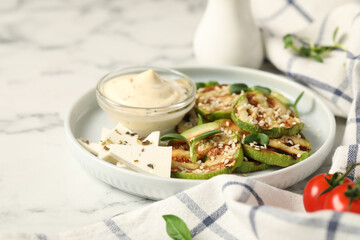 Delicious grilled zucchini slices served with sauce and cheese on white marble table, closeup