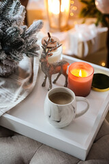 Cup of cocoa, candle and decorative deer on tray at home. Christmas celebration
