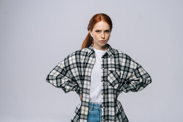 Serious red-haired young woman wearing wireless earphones looking at camera on isolated white background. Pretty redhead lady model emotionally showing facial expressions.