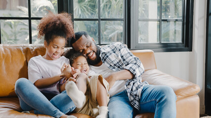 Happy cheerful African American family dad and daughter having fun cuddle play on sofa while birthday at house. Self-isolation, stay at home, social distancing, quarantine for coronavirus prevention.