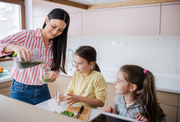 Mother with girls indoors at home, preparing fruit smoothie drink.