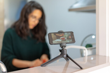 Gravando un videotutorial en la cocina con el móvil sobre un trípode para redes sociales.