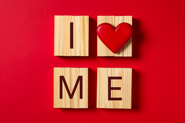 Phrase I Love Me made with wooden cubes and heart on red background, flat lay