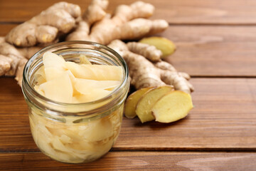 Spicy pickled ginger and root on wooden table, space for text