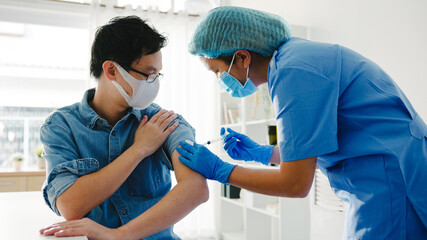 Young Asia lady nurse giving Covid-19 or flu antivirus vaccine shot to senior male patient wear face mask protection from virus disease at health clinic or hospital office. Vaccination concept.