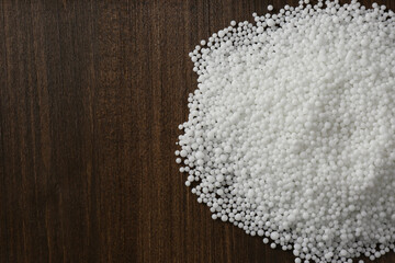 Pellets of ammonium nitrate on wooden table, flat lay with space for text. Mineral fertilizer