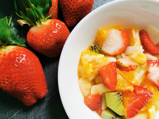Bowl of fresh fruit salad surrounded by assortments of freshly prepared fruits.