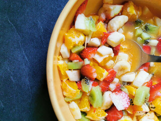 Bowl of fresh fruit salad surrounded by assortments of freshly prepared fruits.