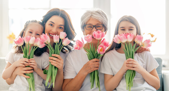 Happy women's day! Child daughters are congratulating mom and granny giving them flowers tulips. Grandma, mum and girls smiling and hugging. Family holiday and togetherness.