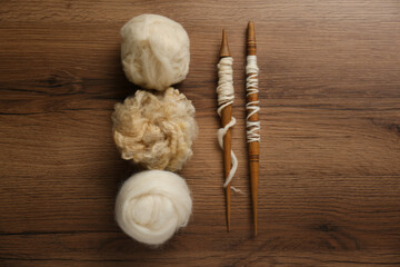 Soft white wool and spindles on wooden table, flat lay