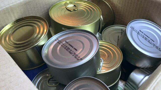 Collect food and groceries in a box for donations and help to the elderly - A man collects a box of humanitarian aid for the needy: rice, cereals, canned goods in tins.