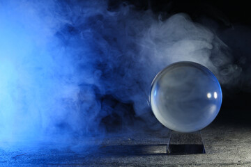 Magic crystal ball  on grey table and smoke against dark background, space for text. Making...