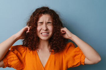 Unhappy ginger woman grimacing and plugging her ears