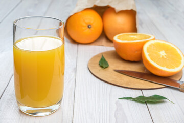Orange juice in a glass on a wooden table, fresh cut oranges in the background
