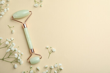 Natural face roller and flowers on beige background, flat lay. Space for text