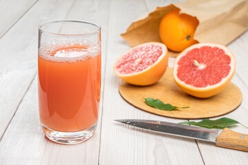 Grapefruit juice in a glass on a wooden table, fresh cut oranges in the background