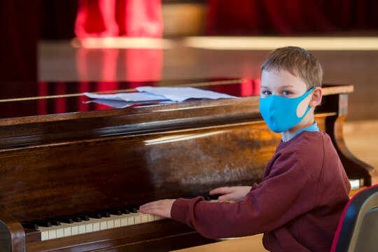Boy wearing a blue mask and playing the piano at lesson and event. Kids back to school concept.
