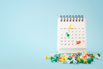 thumbtacks marked on white calendar page with blurred others on grunge blue paper background , due date ,appointment, payment, reminder or business concept