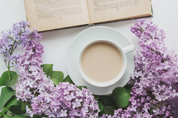spring composition flat lay white cup of coffee, pink lilac beautiful bouquet of lilacs, old book, concept of spring and comfort 