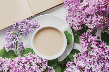 spring composition flat lay white cup of coffee, pink lilac beautiful bouquet of lilacs, old book, concept of spring and comfort 