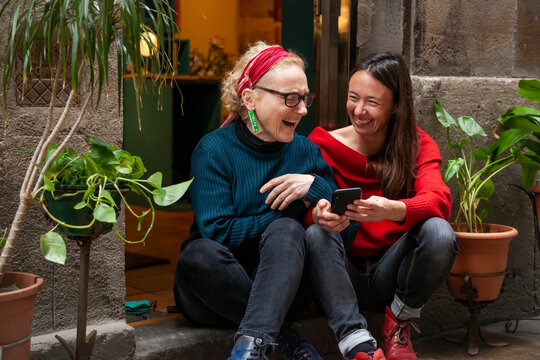 Candid portrait of two female friends chatting, laughing and using a smart phone