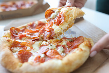 Man taking piece of pizza with sausage and cheese in his hand closeup