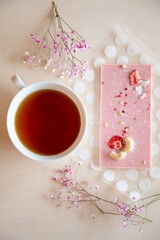 Handmade chocolate with fresh and dried fruits and cup of hot tea on light wooden table with flower