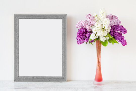 Fresh branches of light pink, purple, white lilac blossoms in vase on table at gray wall. Empty place for inspirational, emotional, sentimental text, lovely quote or sayings in frame. Front view.